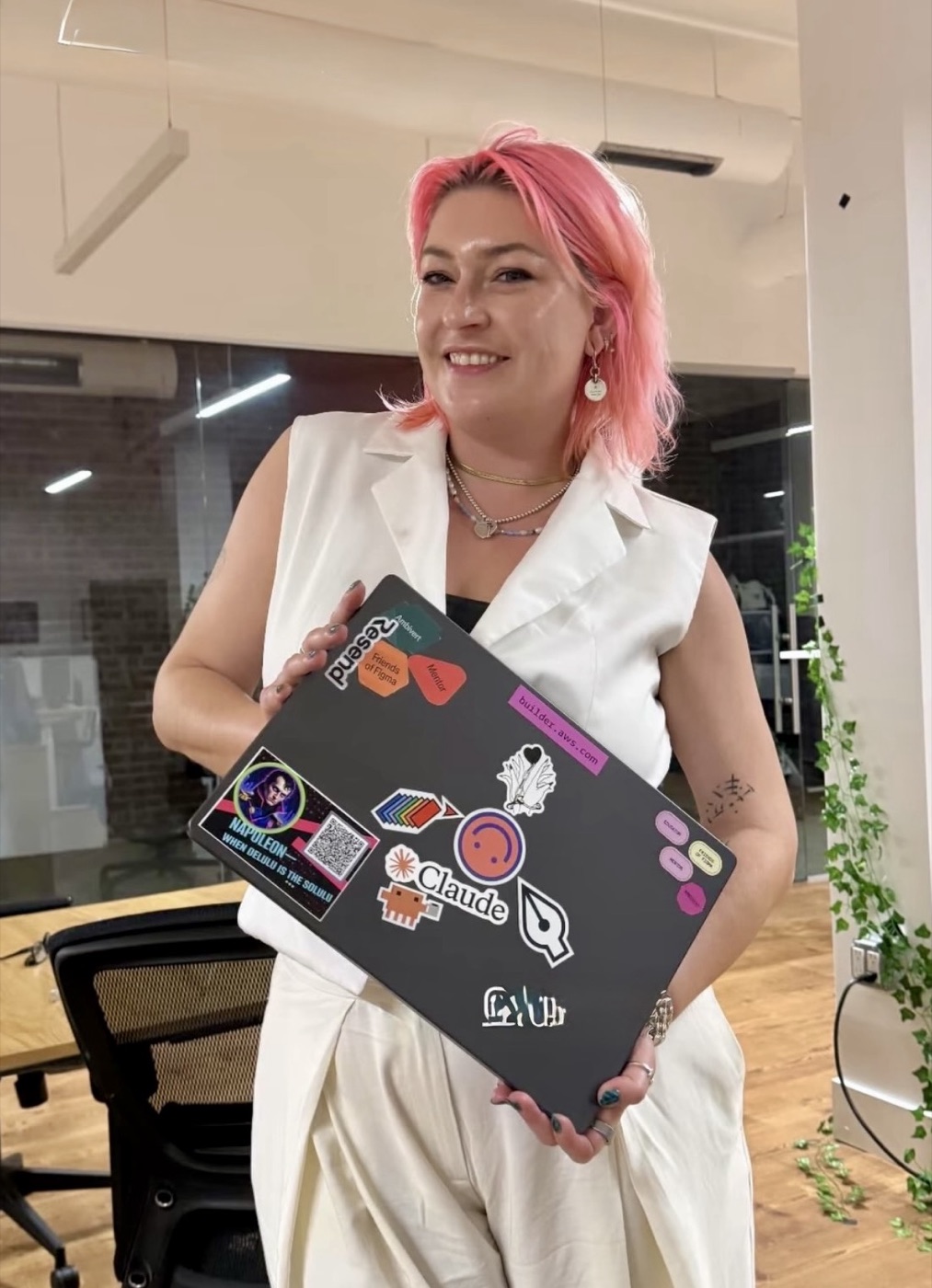 Kate Huezo holding a sticker-covered laptop, pink hair, big smile